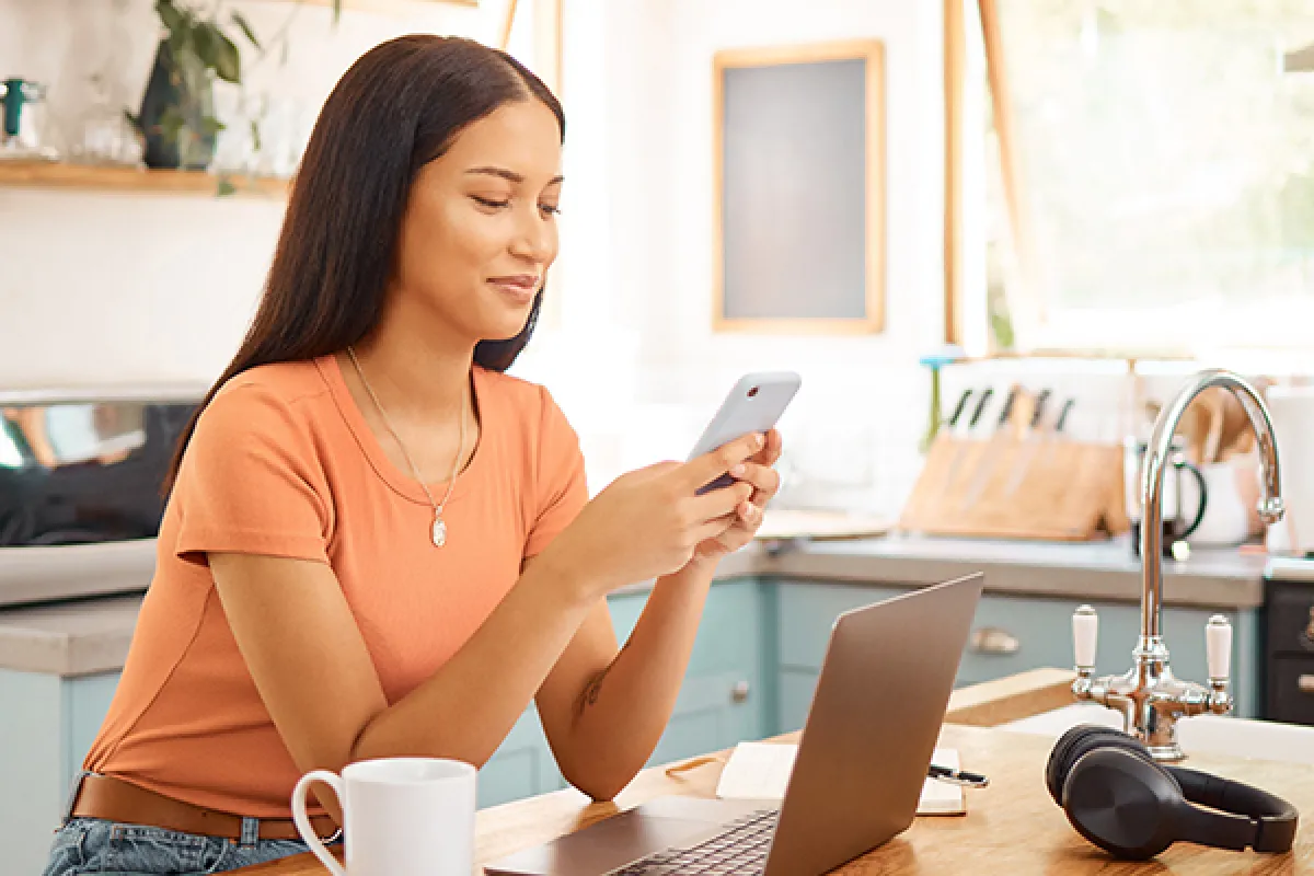 Woman sitting at kitchen bench with mobile phone and lap top.